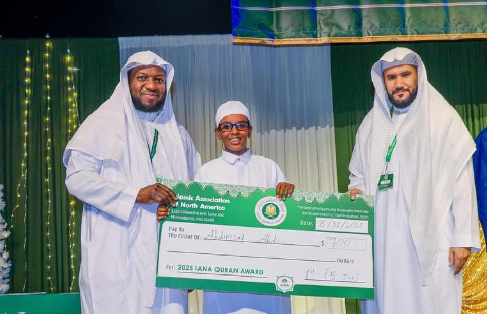 A student on stage receiving the 2025 IANA Qur'an Award check with two teachers