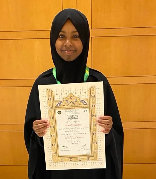 A young student holding her certificate in front of a wooden wall